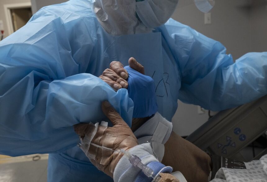 Profissional de saúde e paciente com Covid-19 na UTI se dão as mãos enquanto cama é reposicionada em um hospital de Houston